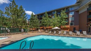 A swimming pool with lounge chairs and a building with balconies in the background. - Ski-In King Executive Resort Suite w/ Mtn Views, Pool & Garage! (Mammoth Lakes)