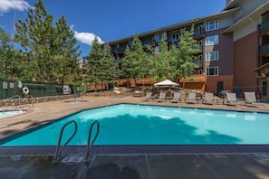 A swimming pool with lounge chairs and a building with balconies in the background. - Ski-In King Executive Resort Suite w/ Mtn Views, Pool & Garage! (Mammoth Lakes)