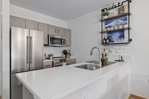 A modern kitchen with stainless steel appliances, a white countertop, and a built-in sink. - Ski-In King Executive Resort Suite w/ Mtn Views, Pool & Garage! (Mammoth Lakes)