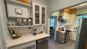 A kitchen with white cabinets, a coffee maker, and a refrigerator. - The Natty - Charming 3BR Bungalow Near UF, The Swamp & Law School (Gainesville)
