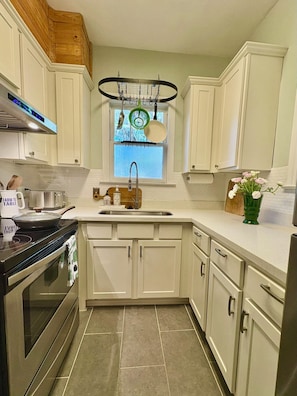 A kitchen with white cabinets, a stainless steel sink, a stove, and a window with a view. - The Natty - Charming 3BR Bungalow Near UF, The Swamp & Law School (Gainesville)