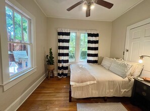 Ein Schlafzimmer mit einem Bett, einem Deckenventilator, einem Fenster mit Vorhängen und einer Pflanze.