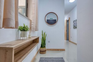 A hallway with a wooden bench, a potted plant, a wall-mounted mirror, and a painting on the wall. - Belmonte Heights Flat 2BDR (Sliema)