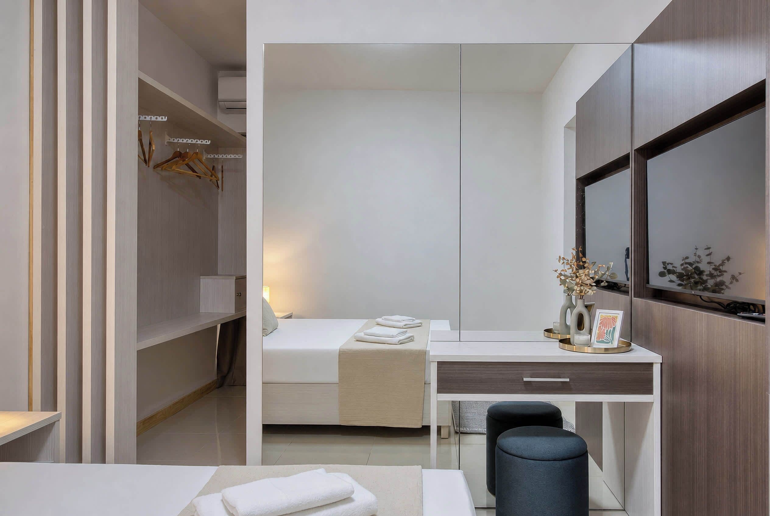 A modern hotel room with a bed, a desk, a chair, and a mirror.