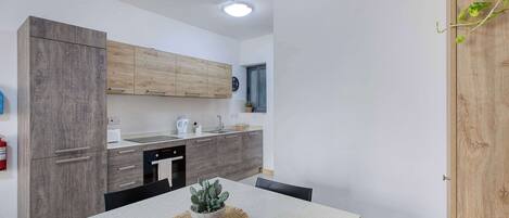 A modern kitchen with wooden cabinets, a built-in oven, and a dining table with a cactus centerpiece.