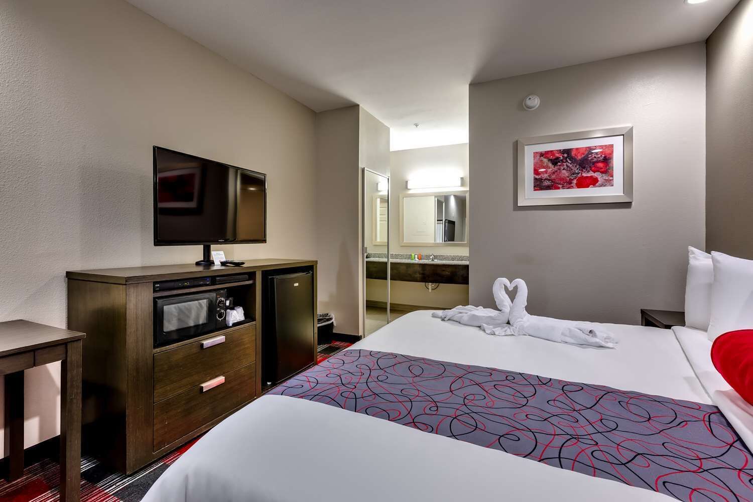 A hotel room with a bed, a desk, a television, a refrigerator, and a bathroom visible through an open door.
