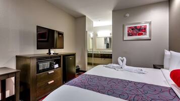 A hotel room with a bed, a desk, a television, a refrigerator, and a bathroom visible through an open door.