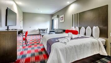 Habitación de hotel con cama, escritorio, televisor y una silla roja.