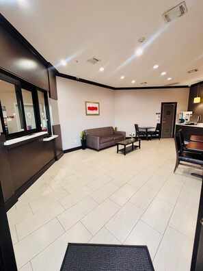 A hotel lobby with a reception desk, a sofa, a coffee table, and a dining area. - Humble Inn & Suites (Humble)