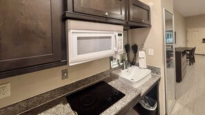A kitchen with dark wooden cabinets, a white microwave, a granite countertop, a sink, and a black stovetop.