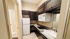 A compact kitchen with a refrigerator, microwave, sink, and dark wooden cabinets. - Humble Inn & Suites (Humble)