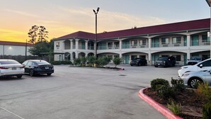 A multi-story motel with a parking lot, several cars parked, and a clear sky. - Humble Inn & Suites (Humble)