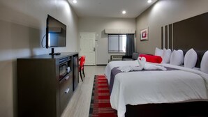 A hotel room with a bed, a desk with a television, a red chair, and a window with curtains.