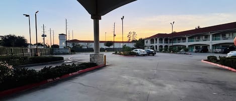 A parking lot with a building in the background, a clear sky, and a sunset.
