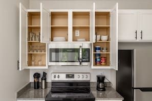 Eine moderne Küche mit weißen Schränken, einem Edelstahl-Kühlschrank, einer Mikrowelle, einem Backofen und einer Kaffeemaschine.