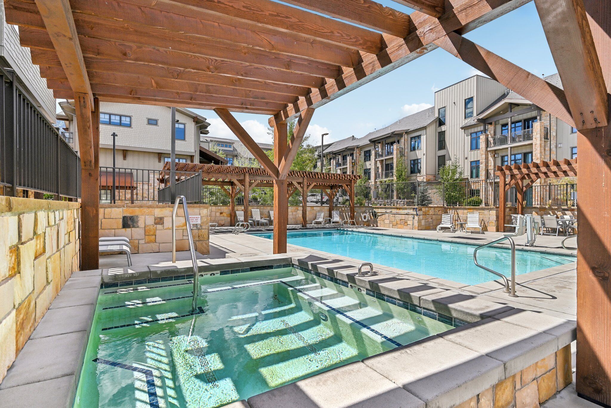 A swimming pool with a wooden pergola overhead, lounge chairs, and a stone wall.