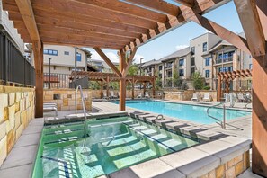 Ein Swimmingpool mit einer hölzernen Pergola darüber, Liegestühlen und einer Steinmauer.