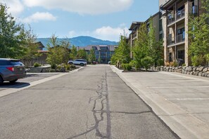 Una calle con coches estacionados, un edificio con balcones y una montaña al fondo.