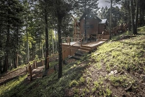 A cabin with a wooden deck, surrounded by forest.