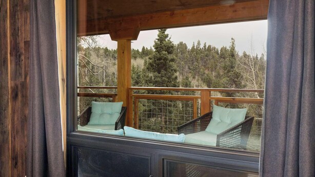 A wooden deck with two wicker chairs and a window overlooking a forested area. - RidgeWalk Lodge and Treehouse - Sleeps 17, Views (Angel Fire)