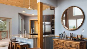 A modern kitchen with a central island, stainless steel appliances, wooden cabinetry, and a large round mirror on the wall. - RidgeWalk Lodge and Treehouse - Sleeps 17, Views (Angel Fire)