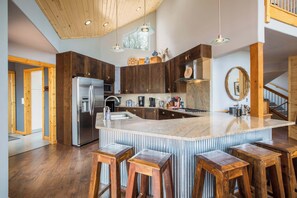 A modern kitchen with a large island, wooden bar stools, and a stainless steel refrigerator. - RidgeWalk Lodge and Treehouse - Sleeps 17, Views (Angel Fire)