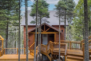Eine Holzjagdhaushälfte mit einer Holzterrasse und einer Treppe, umgeben von hohen Bäumen.