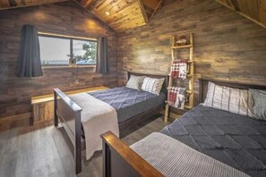 A cozy cabin-style room with two beds, a window with curtains, a wooden ladder, and a view of the outdoors.