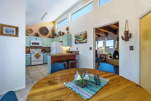 A modern kitchen with teal cabinets, a white stove, and a dining area with a wooden table and blue chairs. - Casa de Colores - Adobe Retreat, Dog-Friendly, AC (Santa Fe)
