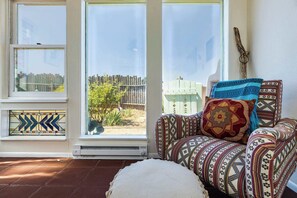 A room with a view of a wooden fence and a tree, a patterned sofa with cushions, and a stained glass window. - Casa de Colores - Adobe Retreat, Dog-Friendly, AC (Santa Fe)