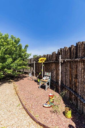 A gravel patio with a wooden fence, a chair, a colorful sculpture, and a sunflower. - Casa de Colores - Adobe Retreat, Dog-Friendly, AC (Santa Fe)