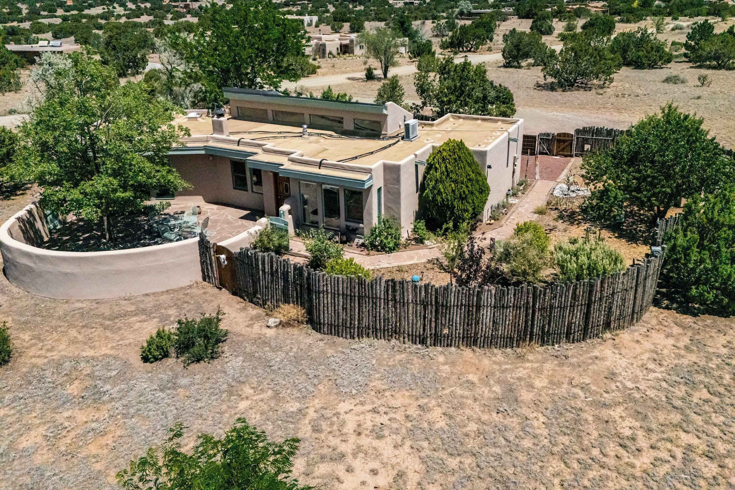 A modern house with a flat roof, surrounded by a wooden fence, and a landscaped garden with trees and shrubs.