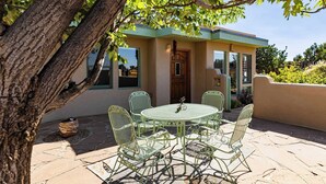 A patio with a round table and chairs, a wooden door, and a view of the sky. - Casa de Colores - Adobe Retreat, Dog-Friendly, AC (Santa Fe)