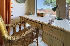 A room with a desk, wicker chair, a lamp, and a view of the outdoors. - Casa de Colores - Adobe Retreat, Dog-Friendly, AC (Santa Fe)