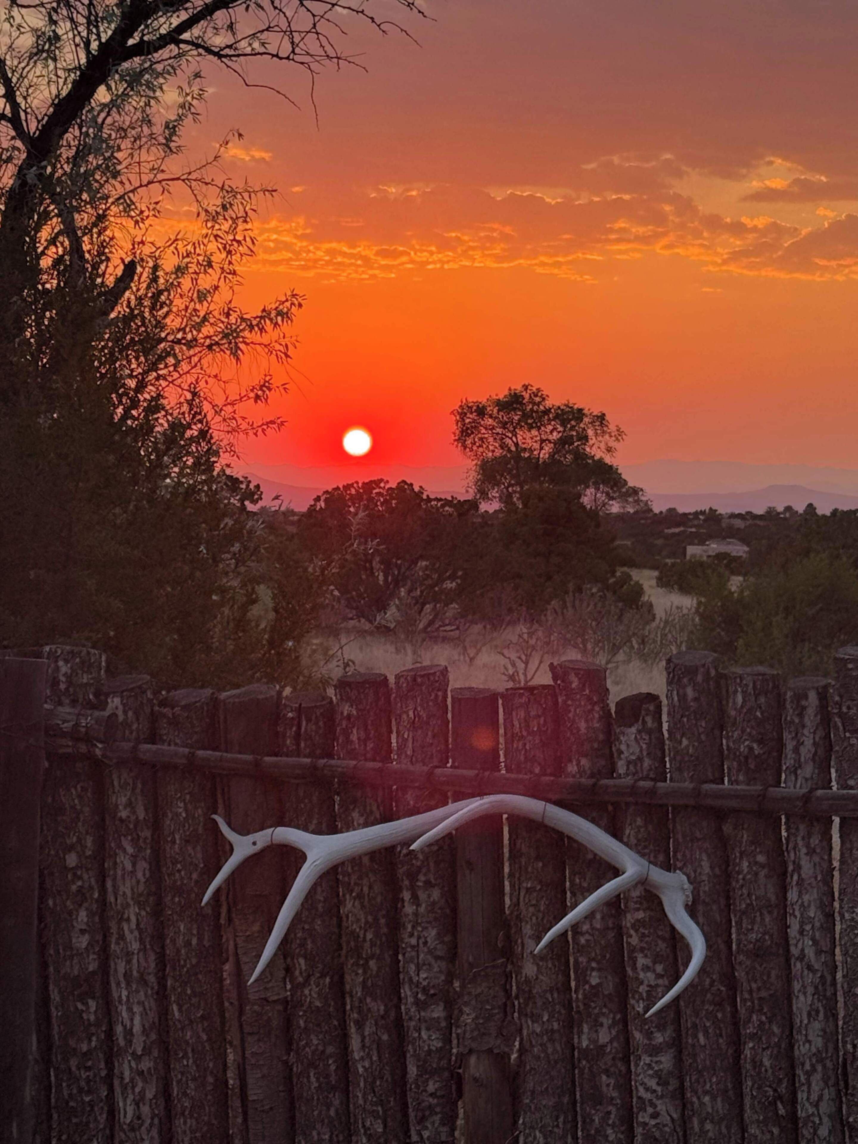 Un atardecer sobre un paisaje con una valla de madera al frente.
