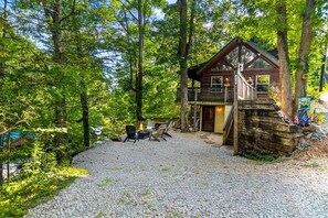 Eine Hütte mit Terrasse, umgeben von Bäumen und einer Schotterzufahrt.