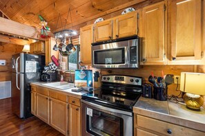 A kitchen with wooden cabinets, stainless steel appliances, and a hanging pot rack. - Cabin at Oak Ridge - Hot Tub, Arcade Game, Firepit + 2 Mi from Downtown Gatlinburg (Gatlinburg)