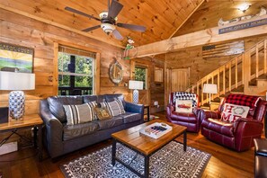 A cozy cabin interior with a wooden ceiling, a leather sofa, a red armchair, and a staircase. - Cabin at Oak Ridge - Hot Tub, Arcade Game, Firepit + 2 Mi from Downtown Gatlinburg (Gatlinburg)