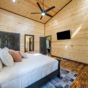 Une chambre à coucher avec un lit, un ventilateur de plafond, un téléviseur à écran plat et des murs en bois.