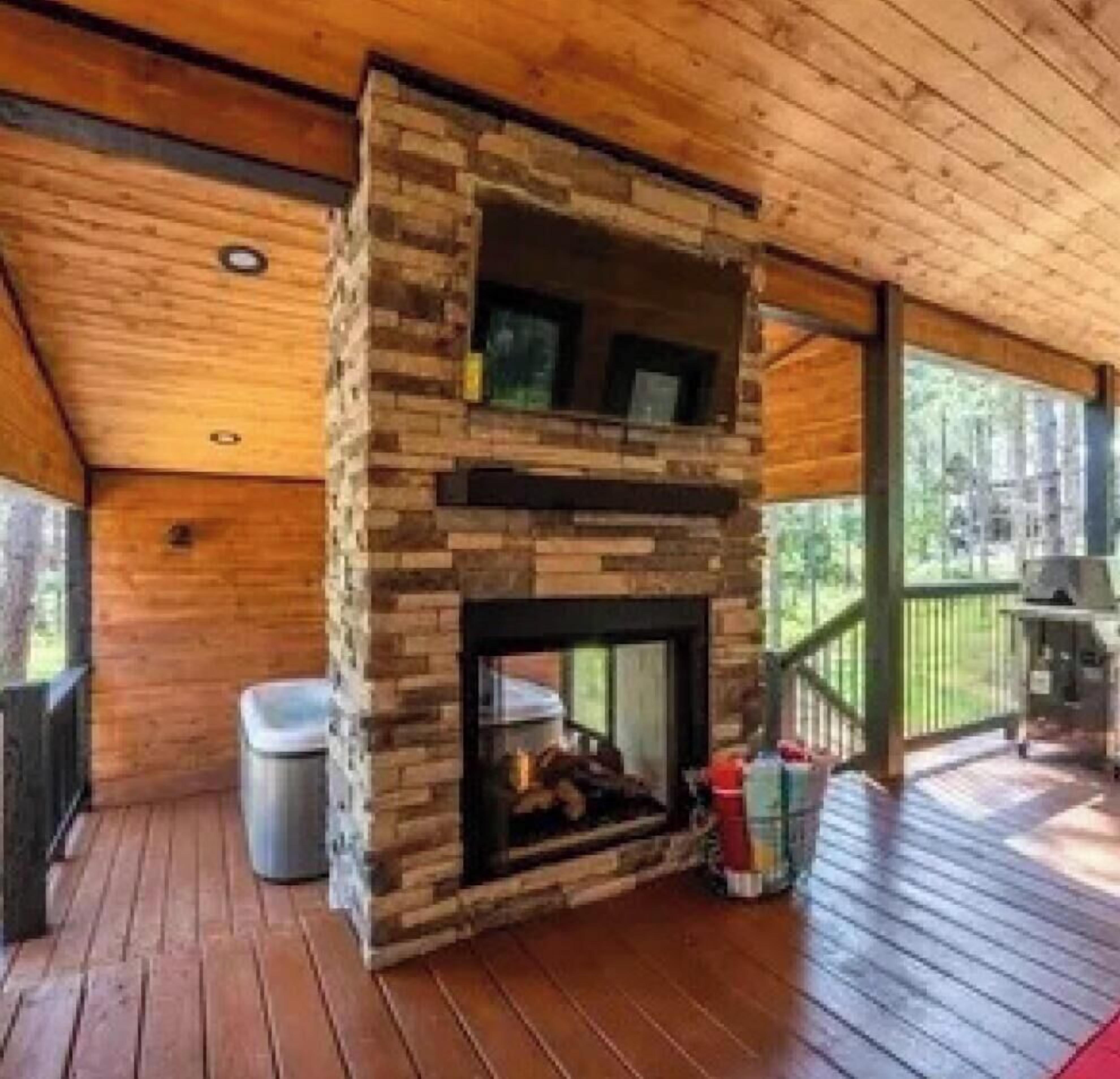 A cabin interior with a stone fireplace, wooden deck, and a view of the outdoors.