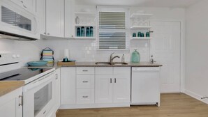 Una cocina moderna con armarios blancos, horno empotrado, pileta y ventana con persianas.