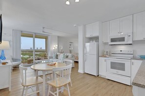 Una cocina moderna con armarios blancos, un microondas y un horno. Hay un comedor con una mesa redonda y sillas.