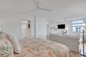 Ein Schlafzimmer mit Bett, Deckenventilator, Bad mit Toilette und einer Küchenzeile mit Fernseher.