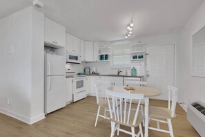 A compact kitchen with white cabinetry, a microwave, a stove, and a dining area with a round table and chairs. - Fresh Coastal-Style Studio | 10th Floor Bay & Gulf Views | Steps to Bonita Beach | Free Parking (Bonita Springs)
