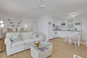 A modern living room with a sofa, coffee table, and a dining area with chairs. - Fresh Coastal-Style Studio | 10th Floor Bay & Gulf Views | Steps to Bonita Beach | Free Parking (Bonita Springs)