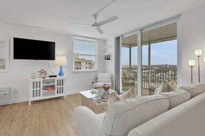 Ein modernes Wohnzimmer mit Flachbildfernseher, weißen Möbeln, Deckenventilator und einem Balkon mit Blick auf die Stadt.