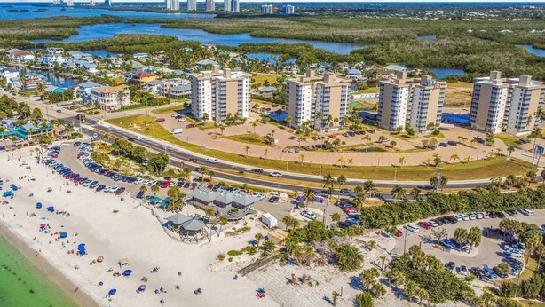 Vista aérea de un complejo turístico costero con edificios altos, una playa con sombrillas y un puerto deportivo.