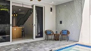 A modern indoor pool area with a glass door entrance, a small seating area with two chairs, and a wooden table. - Park & Palm by Avantstay Private Pool + 4 Ensuite Baths + BBQ Victoria Park + Las Olas (Fort Lauderdale)