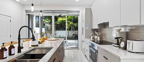 Une cuisine moderne dotée d’un îlot central, d’appareils électroménagers en acier inoxydable et donnant sur un jardin.