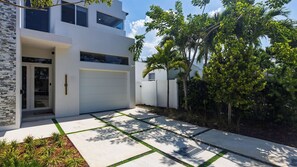 Ein modernes, zweistöckiges Haus mit Garage, Natursteinfassade und gepflegtem Garten mit Palmen.